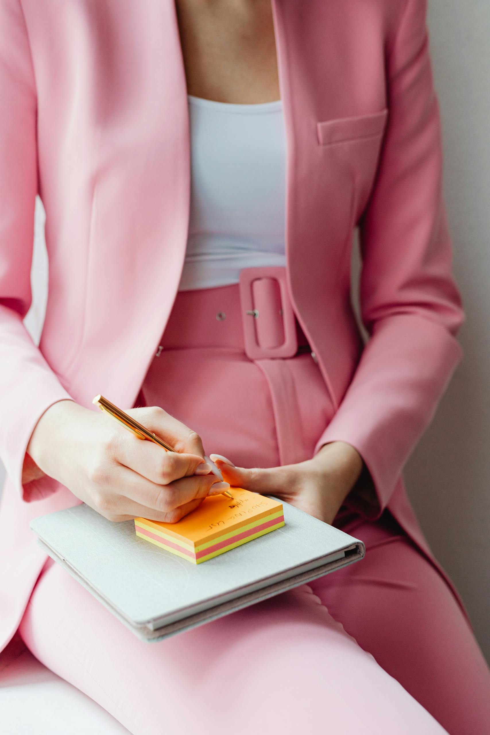 Close-up of a woman in a pink outfit writing notes on sticky notes indoors.